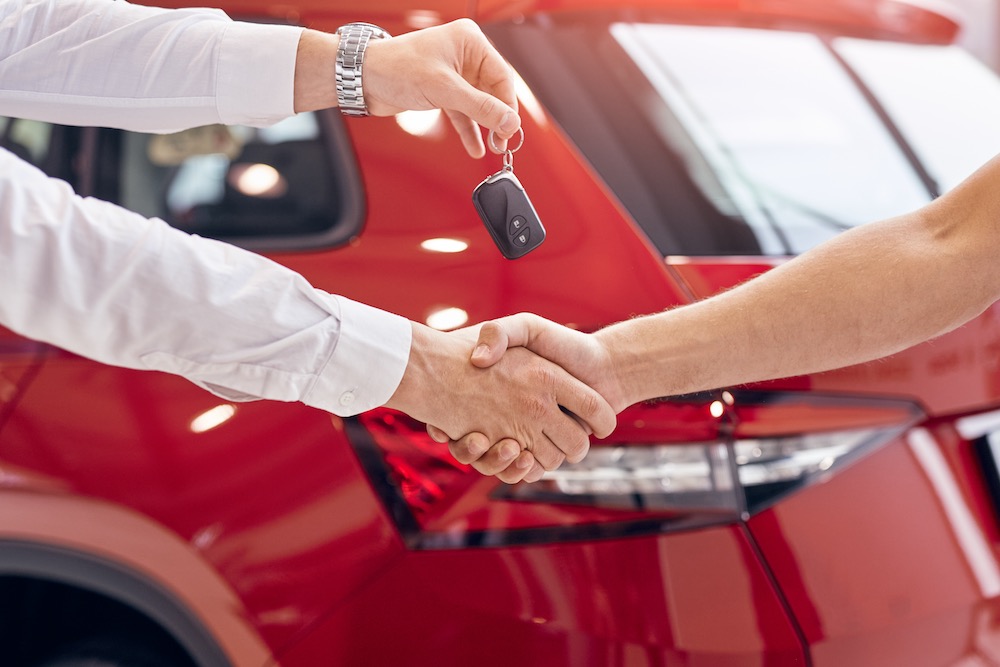 Bilhandlare som räcker över bil och nycklar till köpare